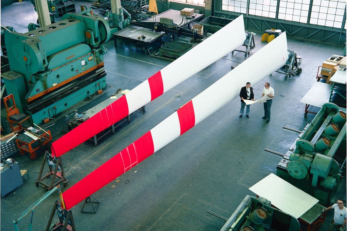 Two men review a drawing on the floor of a metal fabrication shop in Cleveland, Ohio, beside a press brake and two long turbine blades.