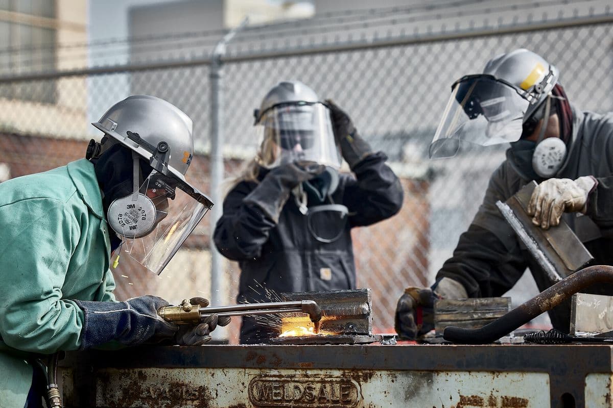 Three workers in face shields and respirators cut and weld steel plate at the Philly Shipyard in Philadelphia, Pennsylvania.