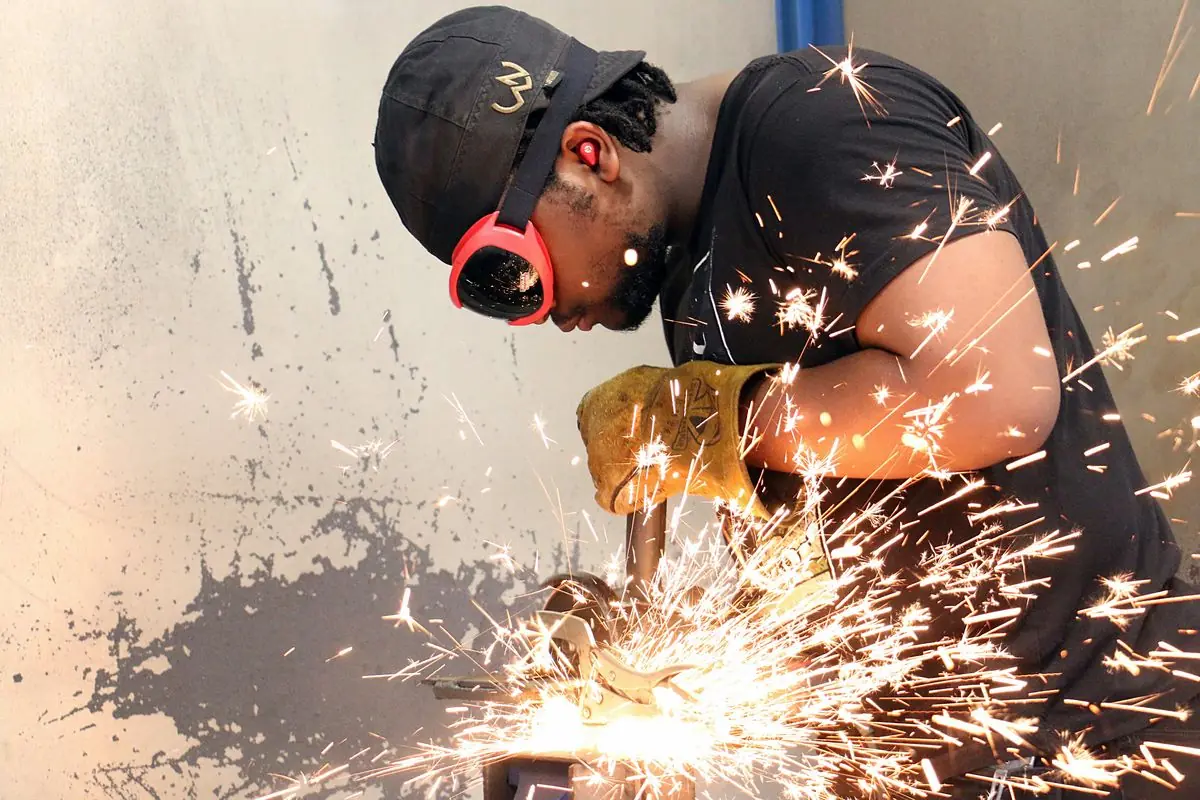 A welding student in ear protection shapes a piece of metal with a grinder as sparks fly in a college shop in Dade City, Florida.