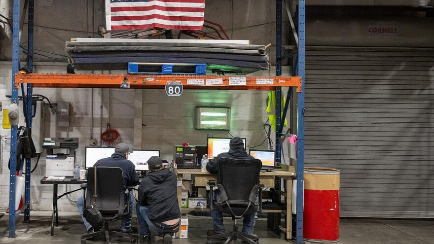 Three staff members work at computer desks set up under the storage racks of a food bank warehouse in central Pennsylvania.